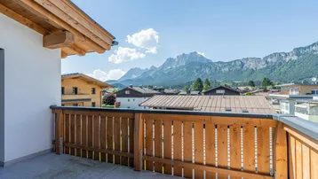 Sonniger Balkon mit Fliesenboden, Holzgeländer und beeindruckendem Bergblick auf die Berge.