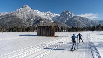 Zwei Langläufer gleiten durch die verschneite Landschaft mit majestätischen Bergen im Hintergrund.