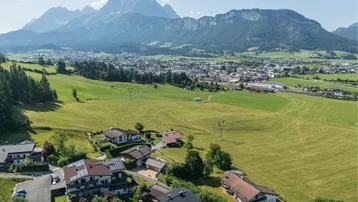 Panoramablick aus der Vogelperspektive auf eine Stadt im Tal, umgeben von Feldern und majestätischen Bergen.