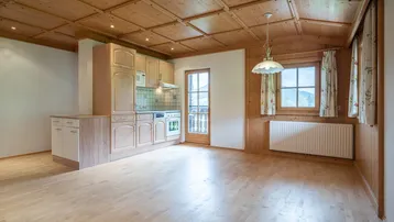 Offener Wohnbereich mit Holzbalkendecke, Einbauküche und Zugang zum Balkon mit Bergblick.