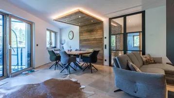Moderner Wohn- und Essbereich mit Holzelementen, bequemer Couch und Zugang zum Balkon.