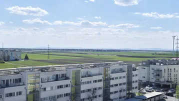 Weitläufiger Ausblick über Wohngebäude, grüne Felder und die ferne Bergkette.