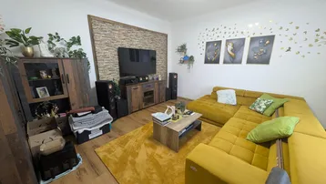Gemütliches Wohnzimmer mit großer gelber Eckcouch, Holzboden und dekorativer Steinwand.