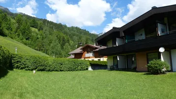 Großer grüner Gartenbereich mit gepflegter Hecke und Blick auf die bewaldeten Berge unter blauem Himmel.
