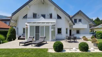 Modernes Einfamilienhaus mit großem Garten, Sonnenterrasse und Wintergarten unter blauem Himmel.