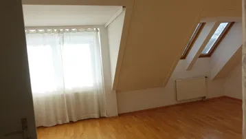 Helles Dachgeschosszimmer mit Holzboden und schrägen Wänden, durchflutet von natürlichem Licht.