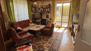 Gemütliches Wohnzimmer mit Ledersofas, Teppichboden und Zugang zu einem Balkon.
