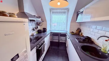 Funktionale Küche mit weißen Schränken, dunkler Arbeitsplatte und Dachschrägenfenster.
