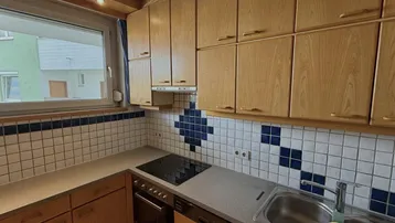 Funktionale Küche mit Holzschränken, Fliesenrückwand und integrierten Elektrogeräten.