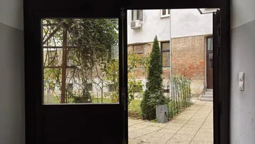 Eingangsbereich mit Glastür, die sich zu einem gepflasterten Innenhof mit Bäumen öffnet.