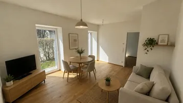 Heller offener Wohn- und Essbereich mit Holzboden, Sofa und Esstisch, durch große Fenster lichtdurchflutet.