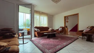 Helles Wohnzimmer mit Fliesenboden, bequemen Sitzgelegenheiten und einem dekorativen Teppich.