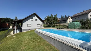 Außenansicht des Hauses mit großem Swimmingpool und gepflegtem Rasen unter blauem Himmel.