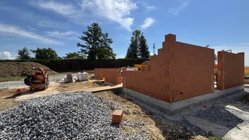 Baustelle mit im Bau befindlichen Ziegelwänden und Baumaterialien unter blauem Himmel.