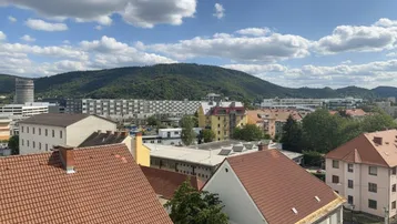 Weitläufiger Blick über die Dächer der Stadt auf bewaldete Hügel und den blauen Himmel.