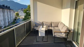 Heller Balkon mit bequemen Outdoor-Möbeln und Blick auf die umliegende Berglandschaft.