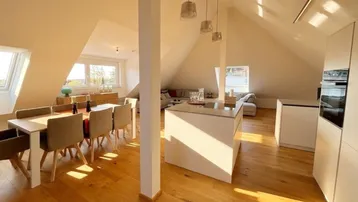 Helles, offenes Dachgeschoss mit moderner Küche, Essbereich und Wohnzimmer, ausgestattet mit Holzboden und schrägen Decken.