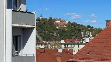 Blick vom Balkon auf die Stadt mit grünen Hügeln und historischen Gebäuden im Hintergrund.