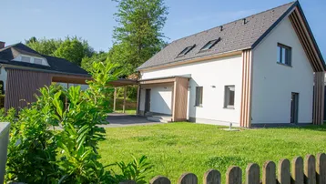 Modernes Einfamilienhaus mit weißer Fassade, Holzakzenten, Carport und einem gepflegten Rasenbereich.