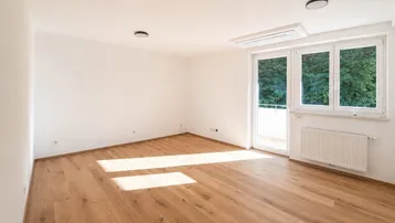 Helles Zimmer mit Holzboden, großen Fenstern und Zugang zu einem Balkon, ideal als Wohn- oder Schlafzimmer.