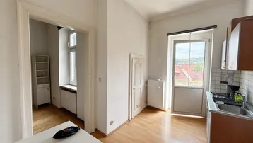 Helle Küche mit Spülbereich, Holzfußboden und Zugang zu einem weiteren Raum.