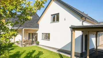 Modernes Einfamilienhaus mit weißer Fassade, Garten und überdachter Terrasse.