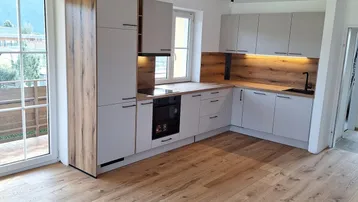 Moderne Einbauküche mit hellgrauen Fronten, Holzakzenten und Zugang zu einem Außenbereich.
