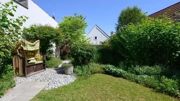Gepflegter Gartenbereich mit Rasenfläche, üppiger Bepflanzung und einem Strandkorb zum Entspannen.