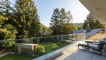 Geräumiger Balkon mit Glasgeländer, Fliesenboden und weitem Blick ins Grüne und auf die umliegenden Häuser.