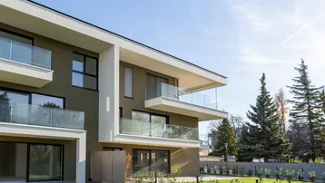 Modernes Mehrfamilienhaus mit großen Balkonen und gepflegter Rasenfläche unter blauem Himmel.