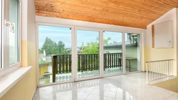 Heller Flur mit glänzenden Fliesen, Holzdecke und Zugang zu einem Balkon mit Weitblick.