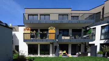 Moderne Wohnanlage mit mehreren Balkonen, dunklen Geländern und einem kleinen Rasenbereich.
