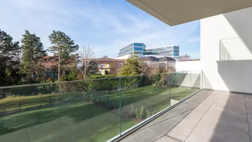 Geräumiger Balkon mit Glasbrüstung und Blick ins Grüne sowie auf entfernte Gebäude.