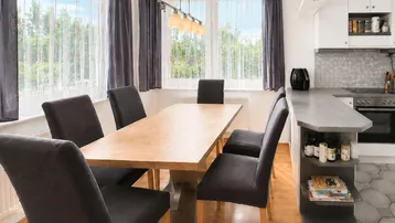 Heller Essbereich mit großem Holztisch und Blick ins Grüne, angrenzend an eine moderne Küche.
