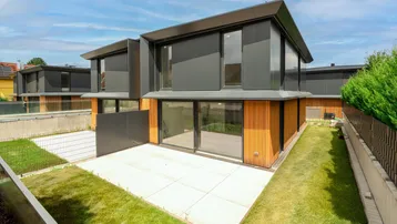 Moderne Doppelhaushälfte mit dunkler Fassade, Holzverkleidung, großer Terrasse und Gartenbereich.