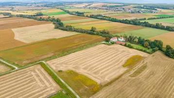 Weitläufige Luftaufnahme der ländlichen Umgebung mit Feldern, Wäldern und Bergen am Horizont.