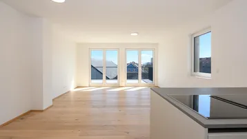 Heller, offener Wohnbereich mit Parkettboden, großen Fenstern und Zugang zu einem Balkon.