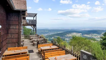 Gemütliche Außenterrasse mit Holztischen und Bänken, die einen weiten Blick über das Tal bietet.