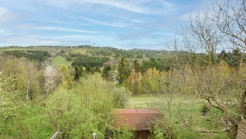 Malerischer Ausblick über die hügelige, grüne Landschaft mit Wäldern und Wiesen.