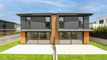 Moderne Doppelhaushälfte mit großen Glasfronten, Holzverkleidung und gepflegtem Rasenbereich.