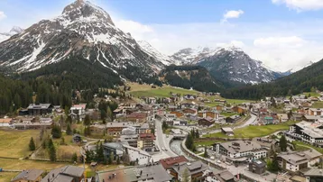 Panoramablick auf ein malerisches Bergdorf, umgeben von schneebedeckten Gipfeln und grünen Wäldern.