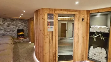 Gemütlicher Wellnessbereich mit Sauna, Entspannungsliege und dekorativem Kamin in Holzoptik.