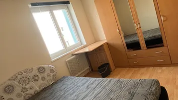 Helles Schlafzimmer mit Holzboden, großem Kleiderschrank und Schreibtisch am Fenster.