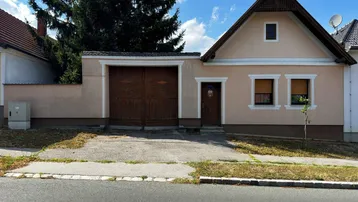 Traditionelles Einfamilienhaus mit angrenzender Garage und einfacher Fassade unter blauem Himmel.