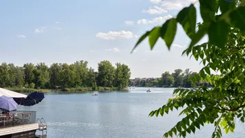 Seeufer mit schwimmender Terrasse und Blick auf die ruhige Wasseroberfläche unter blauem Himmel.