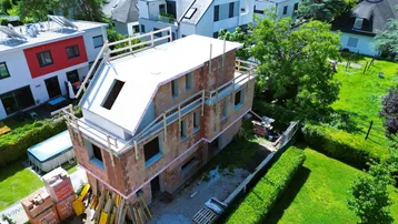 Luftaufnahme eines im Bau befindlichen modernen Einfamilienhauses mit Flachdach und umliegender Grünfläche.
