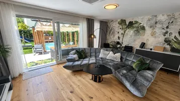 Helles Wohnzimmer mit großem Ecksofa, Holzboden und direktem Zugang zum Garten und Pool.