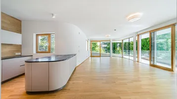 Heller, offener Wohn- und Essbereich mit moderner Küche, Parkettboden und großen Fenstern zur Terrasse.