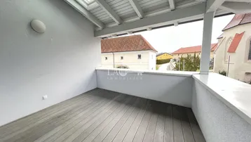 Überdachte Loggia mit Holzboden und Blick auf umliegende Gebäude und den Himmel.