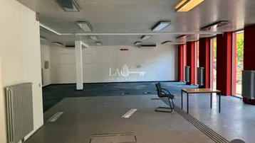Geräumiger Gewerberaum mit großen Fenstern, Teppichboden und Fliesen, ideal für Büro oder Einzelhandel.